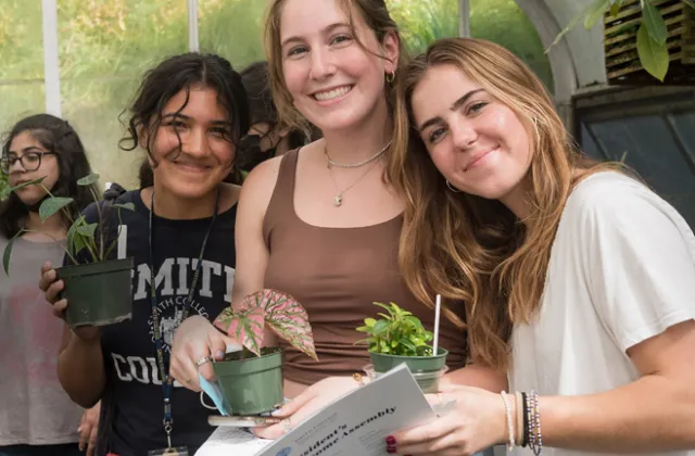 Three new students pick out plants in the greenhouse.