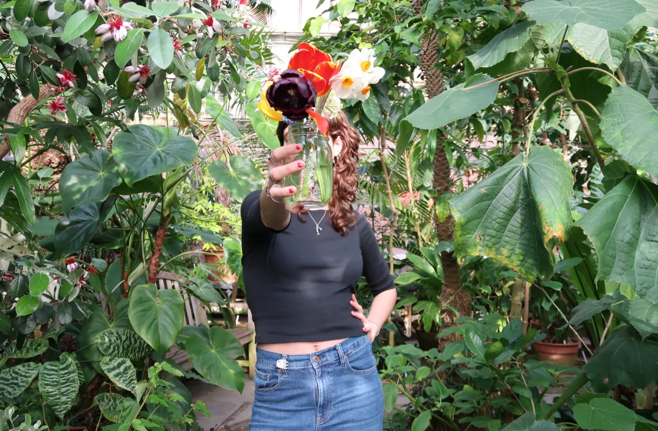 person with black shirt holding mason jar with flower bouquet in front of their face