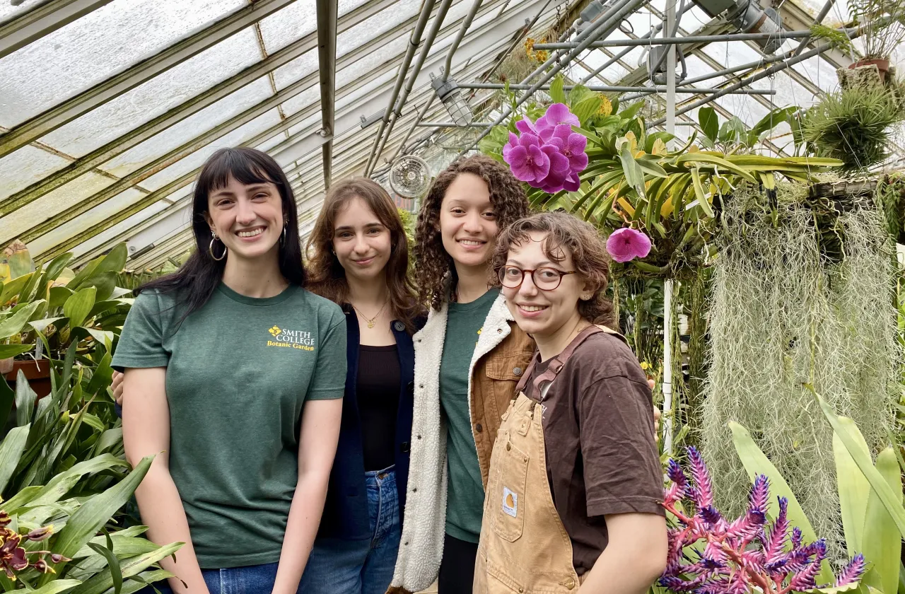 Four students posing for a photo next to pink orchids.