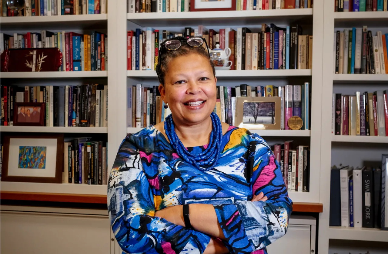 Sarah Willie-LeBreton smiling in front of a bookshelf with her arms crossed