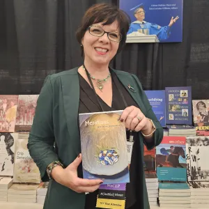 Ginetta Candelario stands in front of the Duke University Press booth at a conference, holding a copy of Meridians.