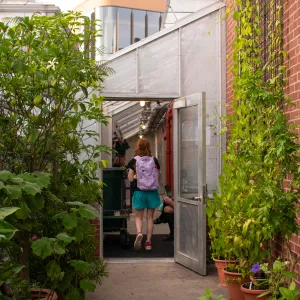 student with purple backpack and green shorts walking through the open back door of the botanic garden
