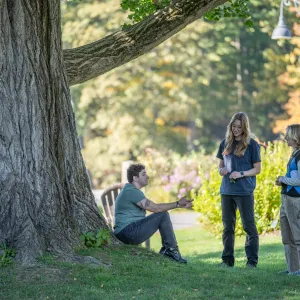 Two students standing and one sitting under a big ginkgo tree.