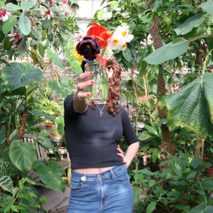person with black shirt holding mason jar with flower bouquet in front of their face