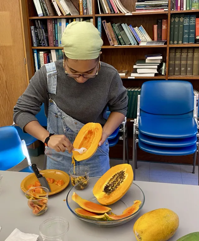 student with yellow bandana and overalls cleaning a papaya in a classroom