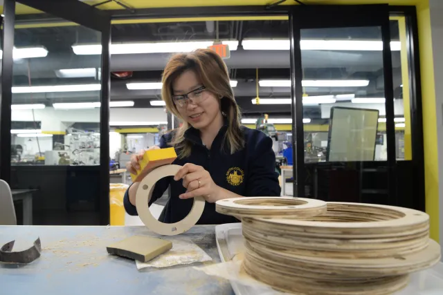 Female student sanding round wood piece with safety googles on
