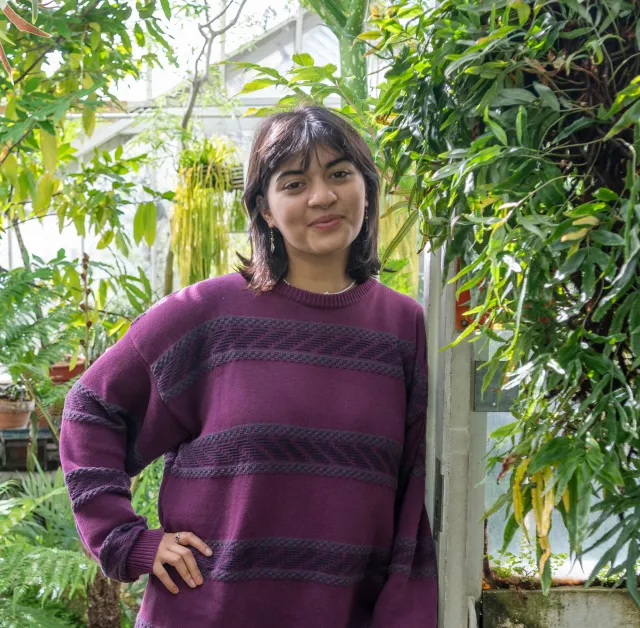 Student with purple sweater and shoulder length hair posing in conservatory.