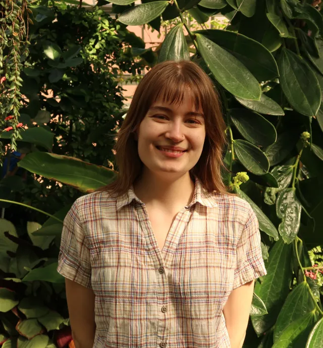 Student with plaid shirt posing in and short light brown hair posing in conservatory.
