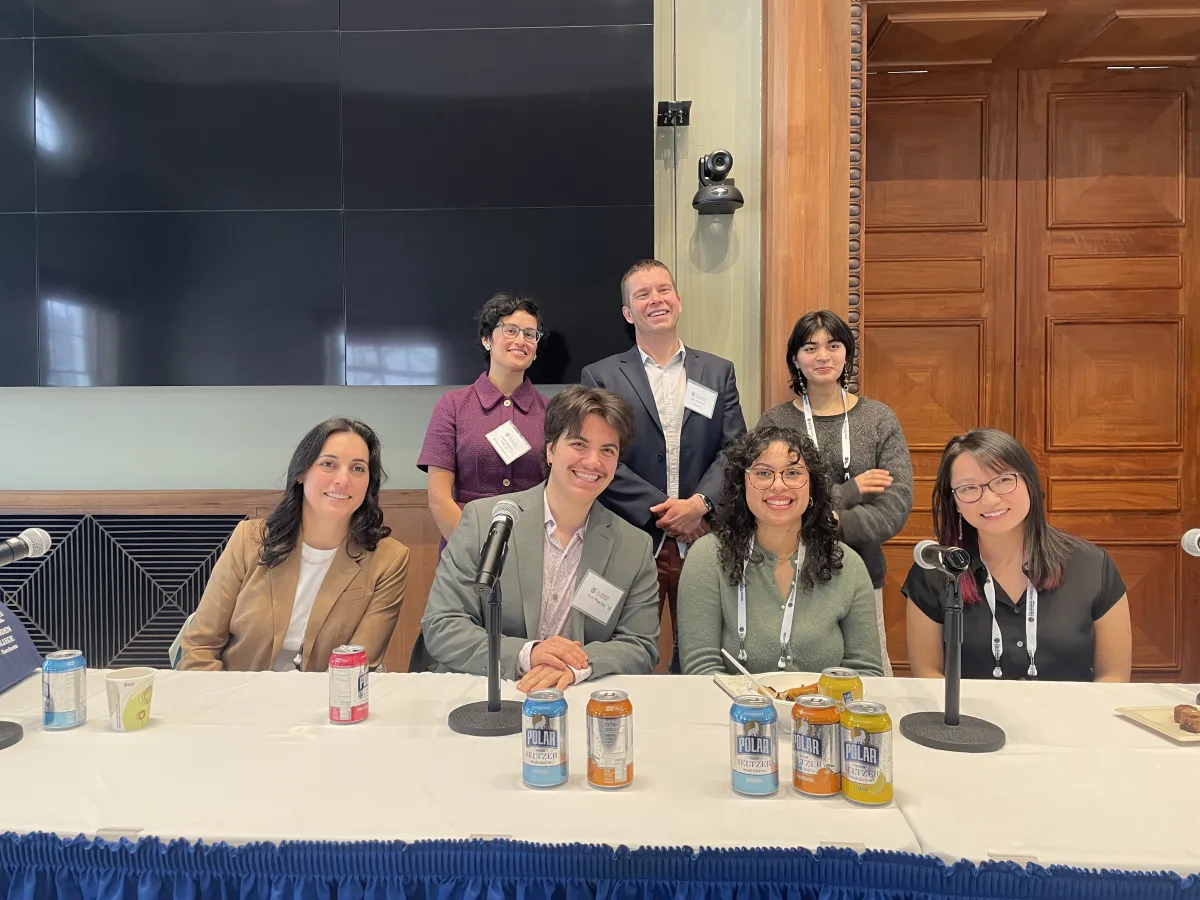 Seven individuals posing for a group photo behind a panel table.