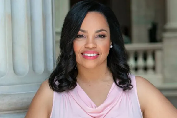 An African American woman in front of marble columns in a pale pink dress.