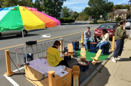 People relax in a portable park on the street, under an umbrella and surrounded by games