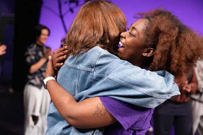 A side-view of two students embraced in a hug, one student smiles enthusiastically.