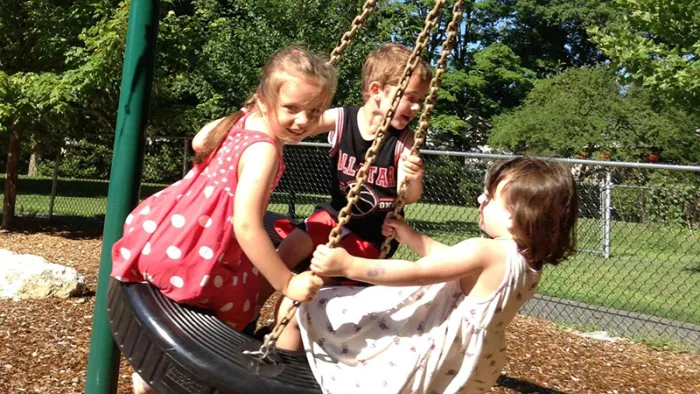 Three children on a tire swing