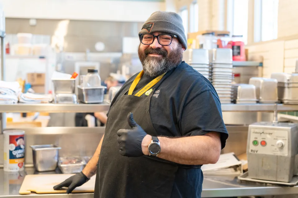 Moises (Moe) Torres, wearing a black apron, smiles in the kitchen