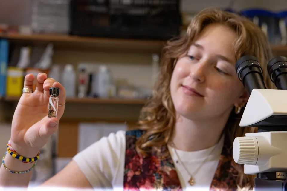 A student holds up a vial with a macroinvertebrate in Professor Marney Pratt's lab