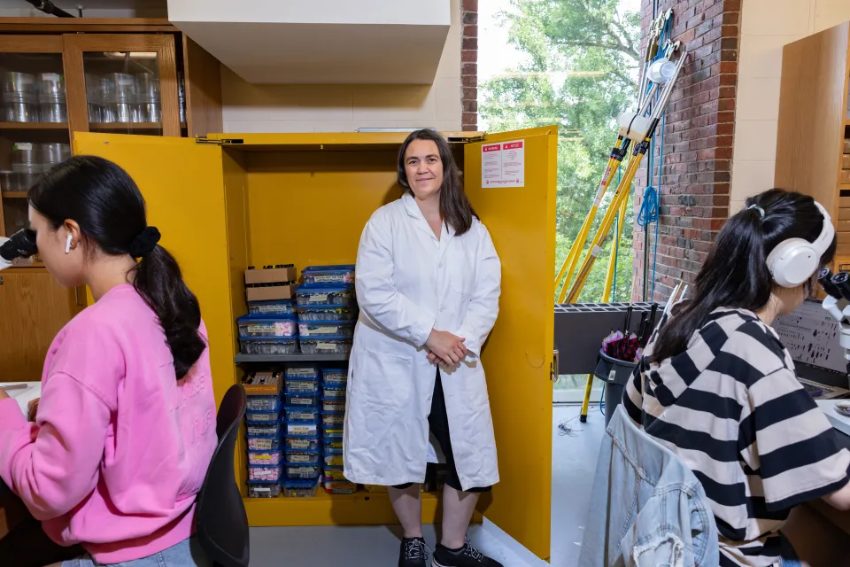 Professor Marney Pratt stands against yellow cabinets in her Sabin-Reed lab with students working on either side