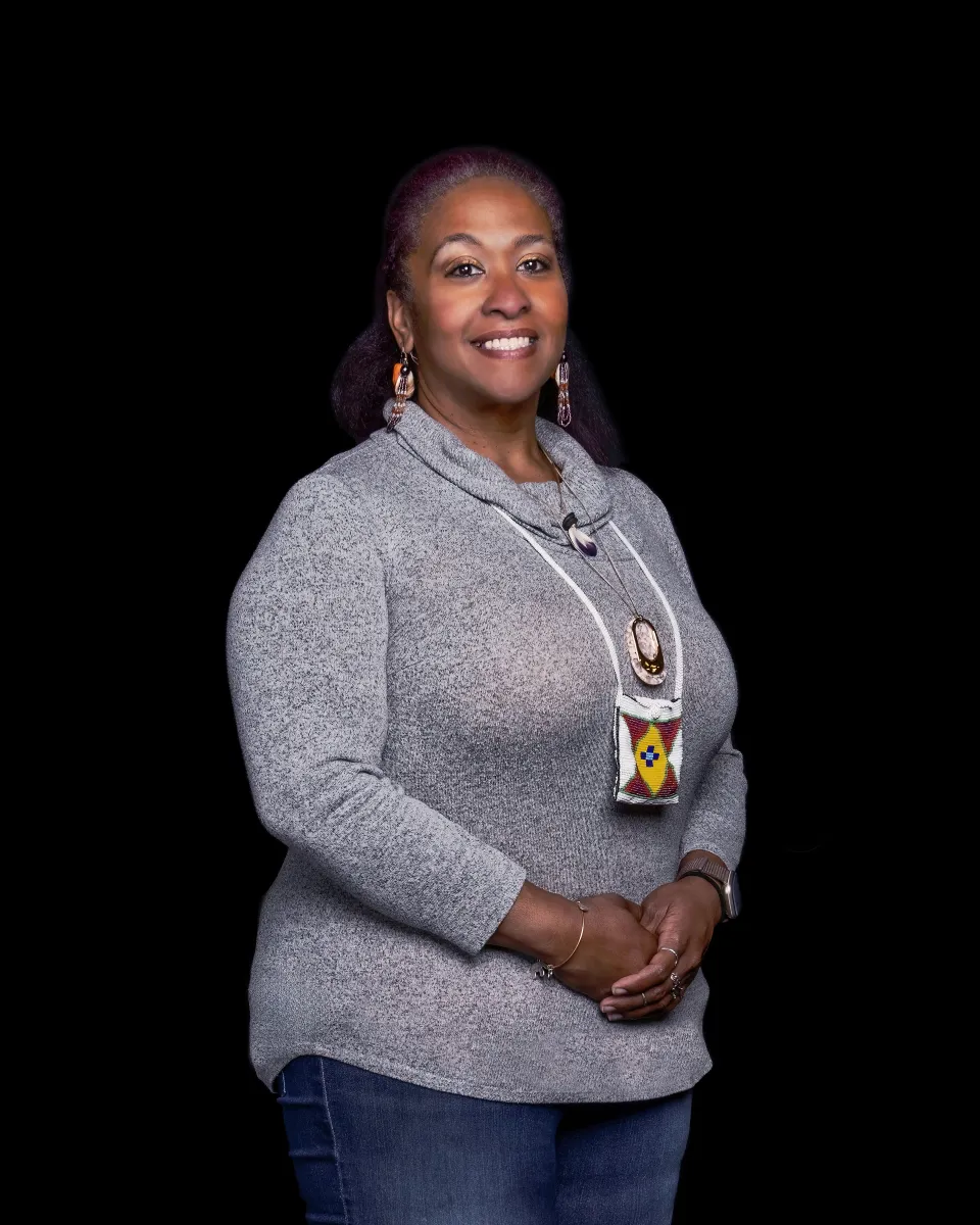 woman in grey shirt and jeans wearing a traditional indigenous necklace on smiling