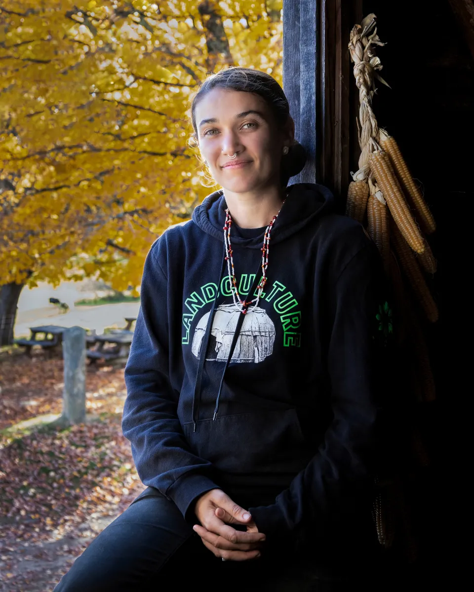 woman sitting in an open barn window in a blue hoodie with brown hair pulled back smiling