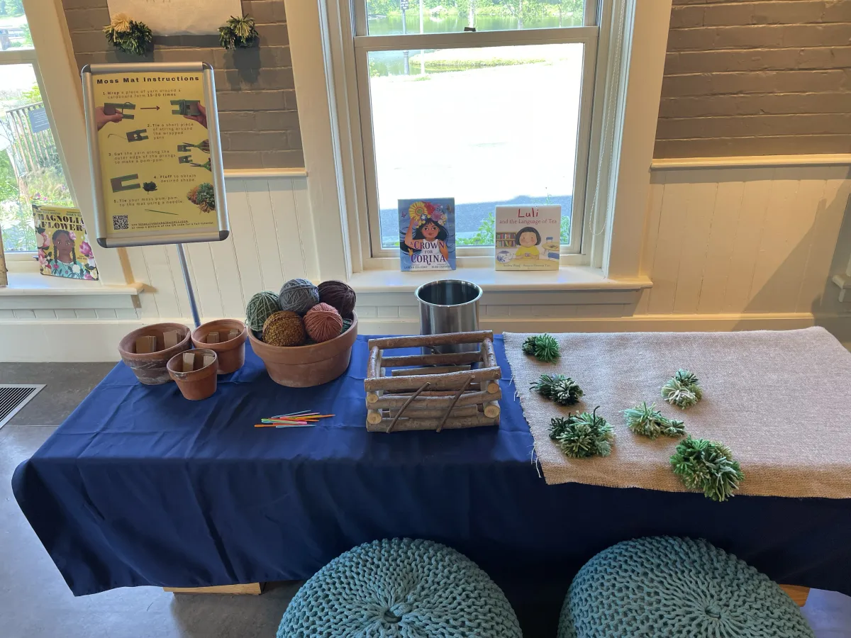 Table with blue table cloth and yarn craft on it.
