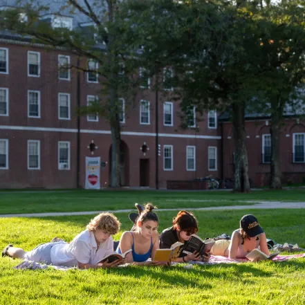 Four students lying in the grass in the Quad, reading books.