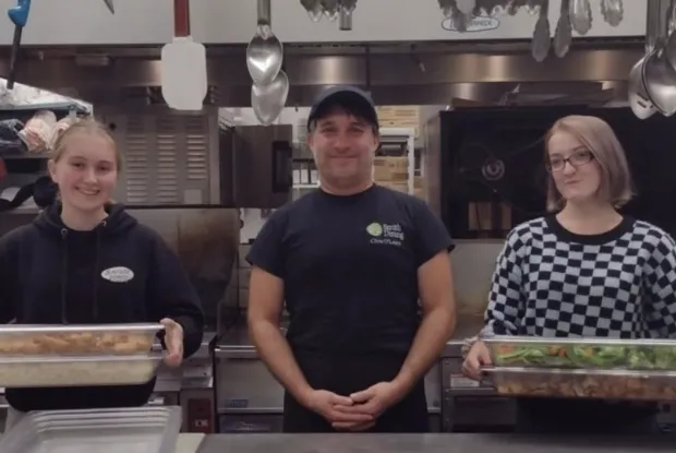 Two students and a staff member pose with food to be donated.