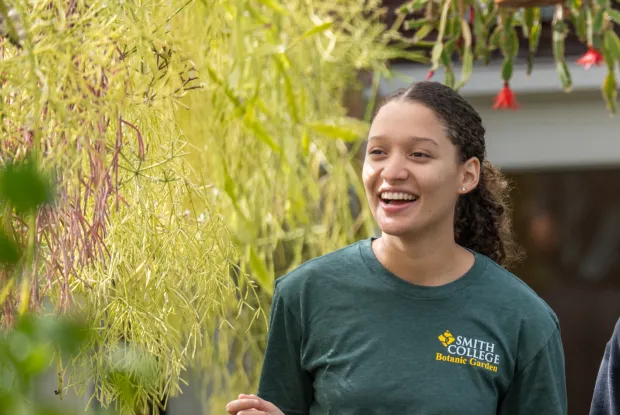 Girl smiling in green shirt walking by plants. 